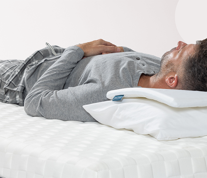 Man lying on his back on a bed, using a white pillow with a foam slice for added support