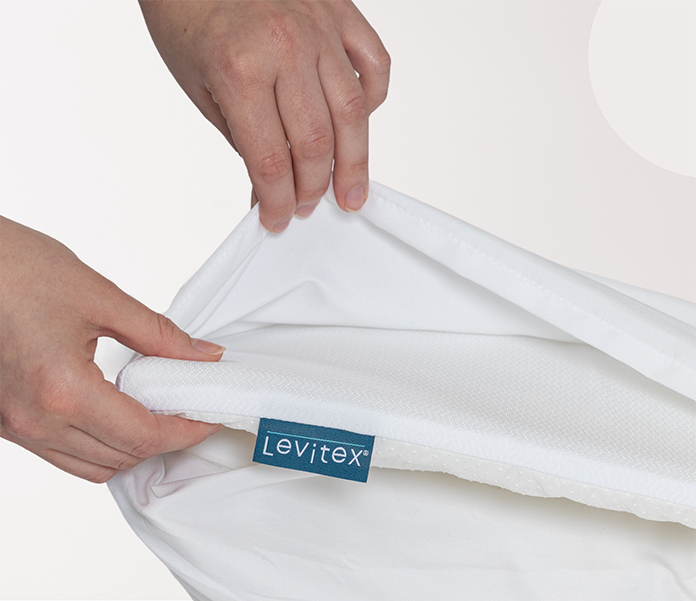 White slice of foam with a Levitex label held by hands against a white background