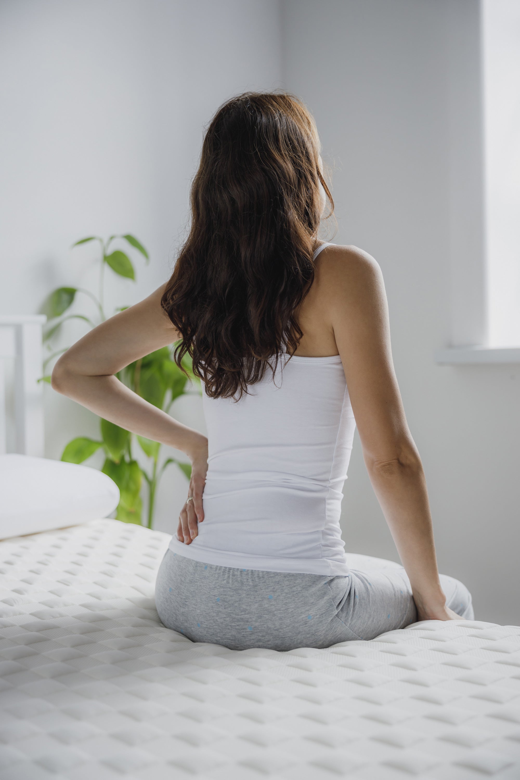 a woman sitting on a bed in pyjamas, holding her lower back